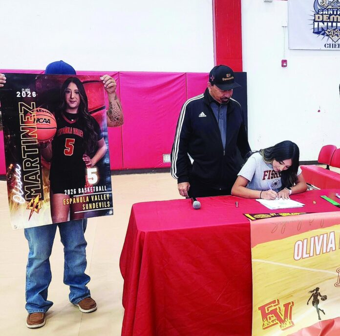 Española Valley point guard Olivia Martinez signs her letter of intent to play basketball at St. John Fisher University Rochester, New York, as coach Ray Romero makes sure she hits the dotted line.