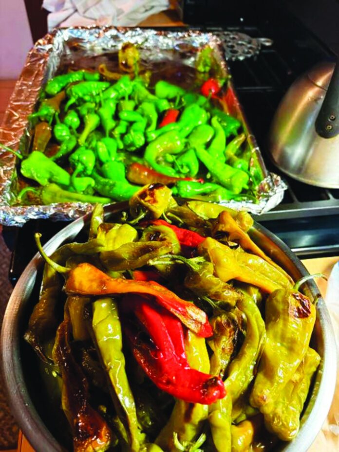 A baking sheet with chile set for roasting and a stainless steel bowl with roasted chile set for steaming.